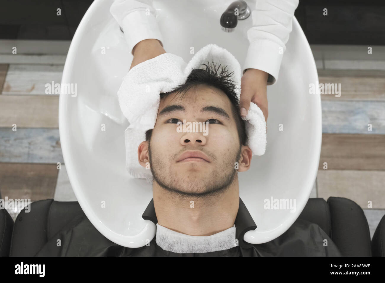 Vue de dessus de l'appareil photo de l'homme asiatique coiffure lave la tête du client et l'essuie avec une serviette. Banque D'Images