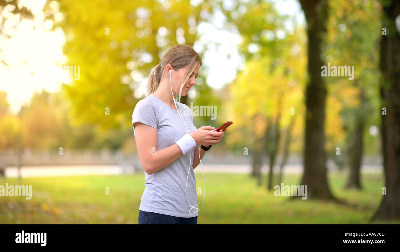 Athlète fille jogging dans le parc le soir. Se reposer et parler sur les réseaux sociaux. Écouter de la musique. D'entraînement. Mode de vie sain. Banque D'Images