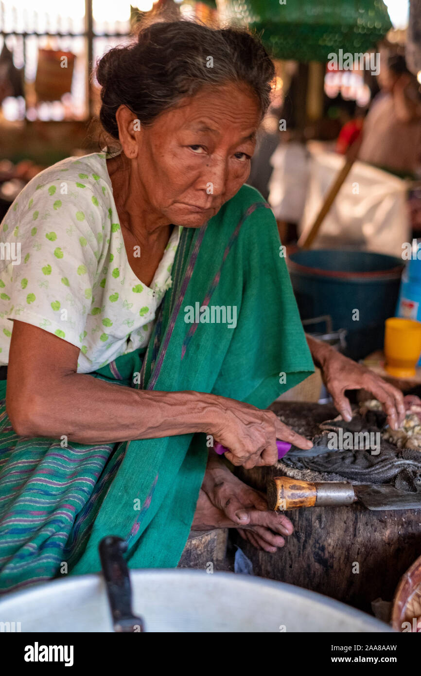 Le quartier animé de viande, poisson, légumes et fruits du marché Pakokku, Myanmar (Birmanie) avec une femme plus âgée la préparation/vendre des fruits de mer avec un froncement de sourcil Banque D'Images