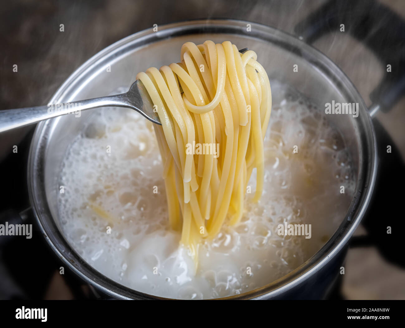 Nouilles jaunes ou spaghettis dans l'eau bouillante de cuisson pot avec piscine un faible éclairage. Banque D'Images