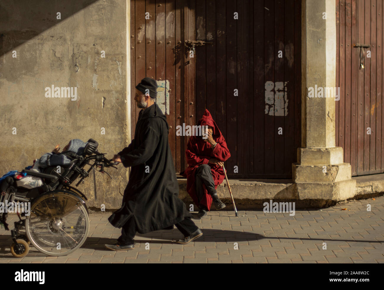 Scène de la vie quotidienne dans la médina de Fès. Vieil homme de soleil pendant ce temps, un père est passant portant son enfant tétraplégique. Banque D'Images