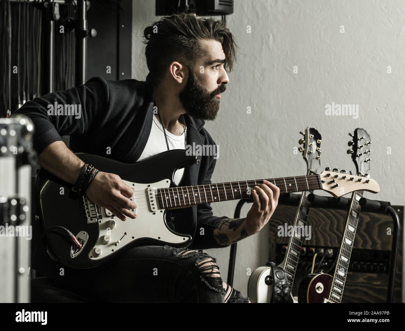 Photo d'un homme à barbe assis et jouant de sa guitare électrique dans un studio d'enregistrement. Banque D'Images