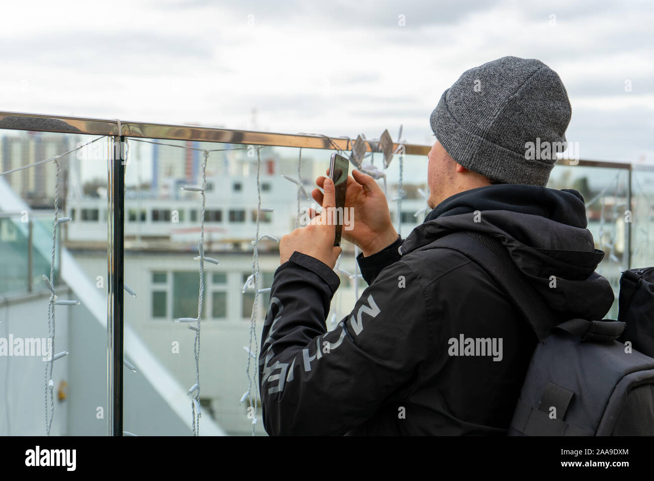 Un homme dans la vingtaine, portant un chapeau de laine à l'aide d'un téléphone mobile ou téléphone cellulaire pour prendre une photo d'une attraction touristique Banque D'Images