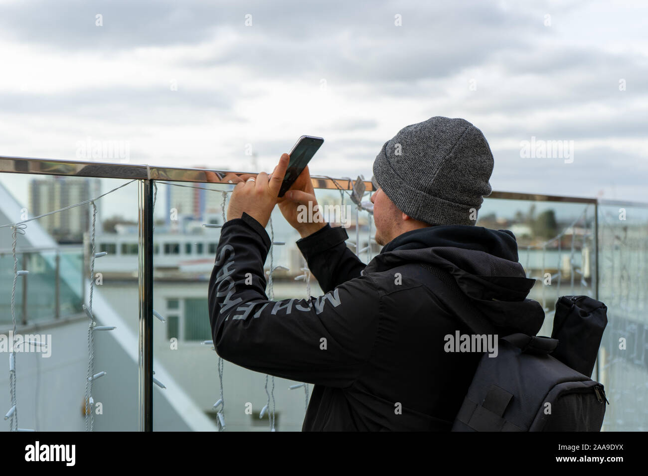 Un homme dans la vingtaine, portant un chapeau de laine à l'aide d'un téléphone mobile ou téléphone cellulaire pour prendre une photo d'une attraction touristique Banque D'Images