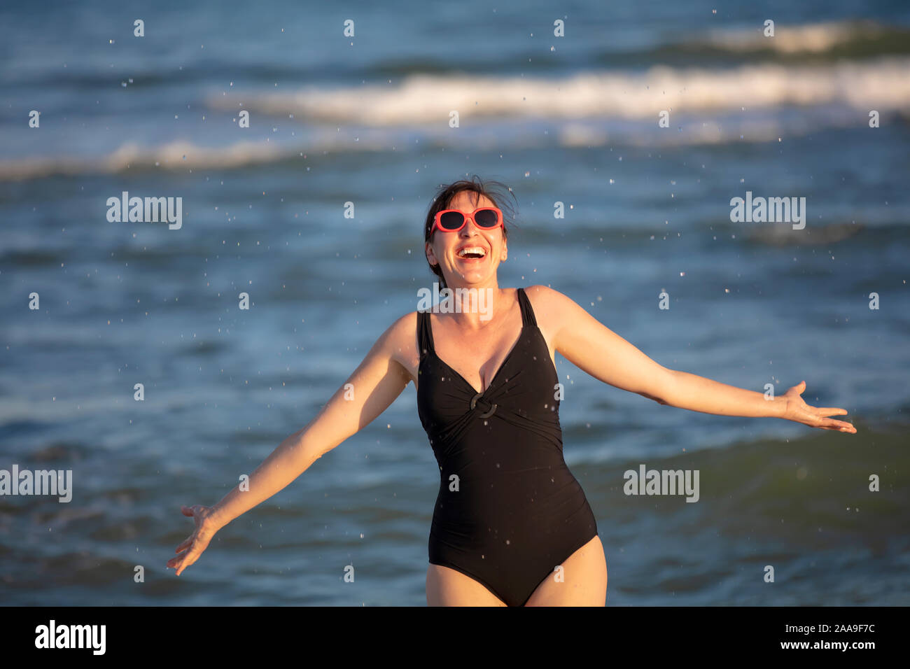 Femme heureuse à la mer. Femme dans un maillot de l'eau éclabousse sur fond de vagues. Vacances d'été sur la plage. Banque D'Images
