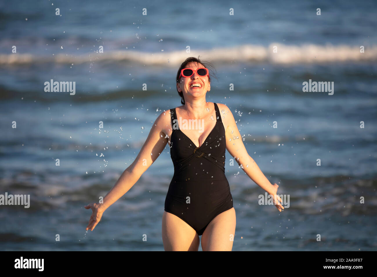 Femme heureuse à la mer. Femme dans un maillot de l'eau éclabousse sur fond de vagues. Vacances d'été sur la plage. Banque D'Images