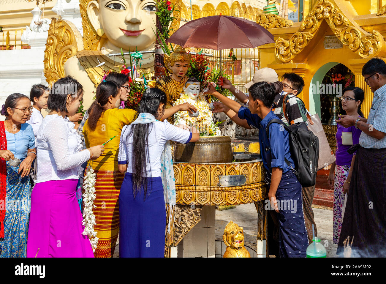 Les gens prennent part à des bouddhistes le rituel de verser de l'eau plus de statues bouddhiques, la pagode Shwedagon, Yangon, Myanmar. Banque D'Images