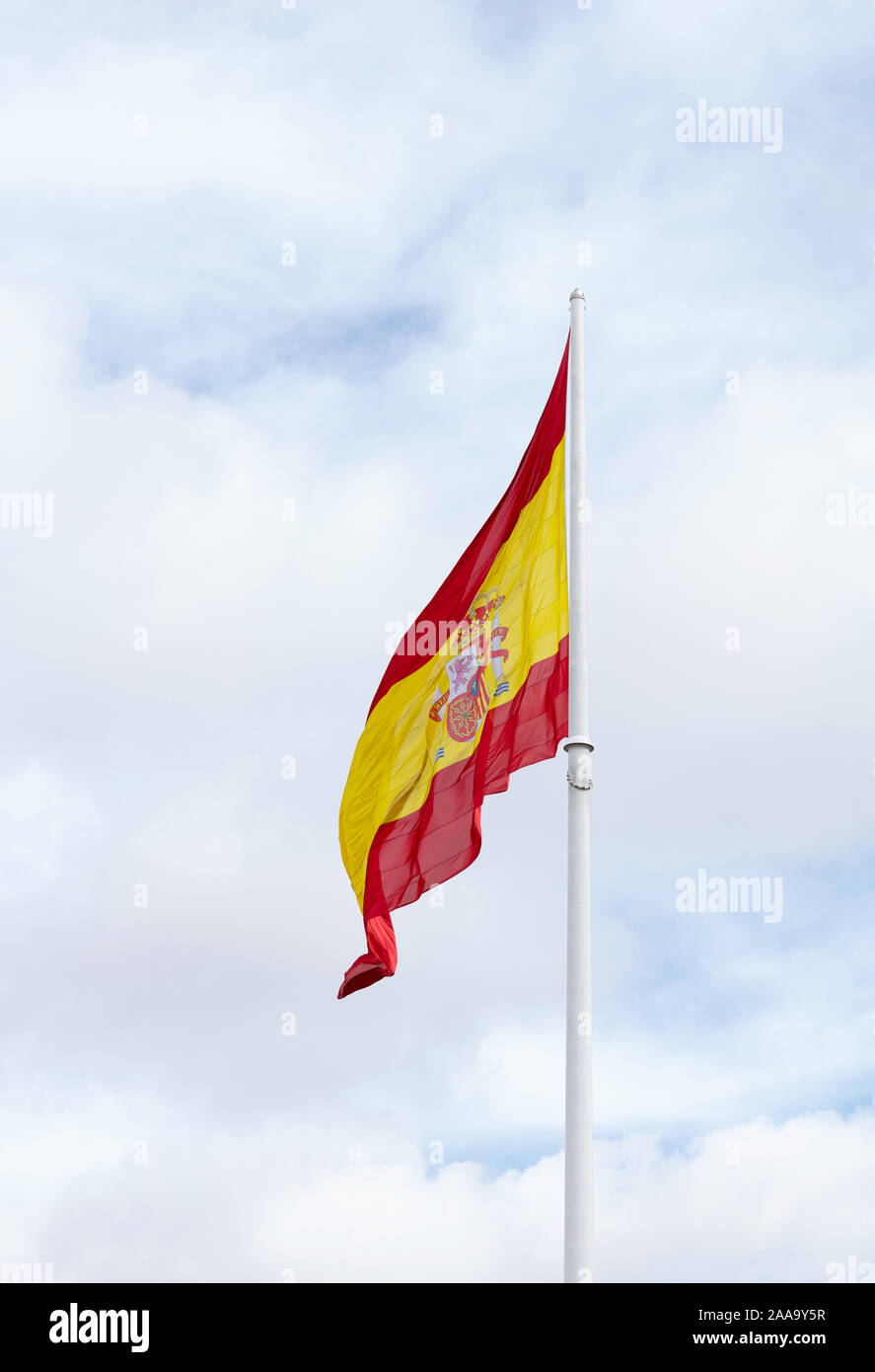 Drapeau espagnol sur un mât blanc forme dans le vent avec un ciel nuageux ciel bleu en arrière-plan Banque D'Images