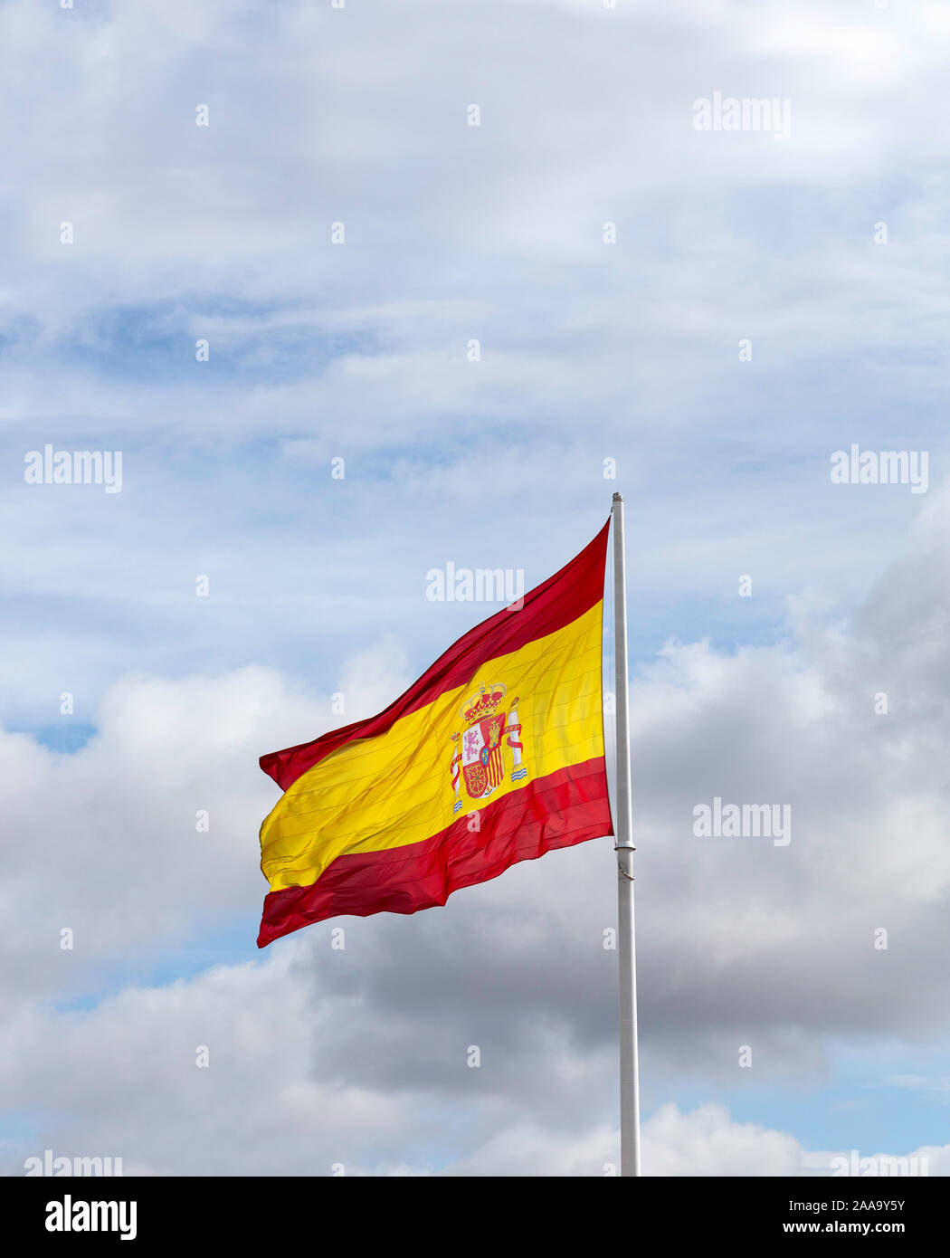Drapeau espagnol sur un mât blanc forme dans le vent avec un ciel nuageux ciel bleu en arrière-plan Banque D'Images