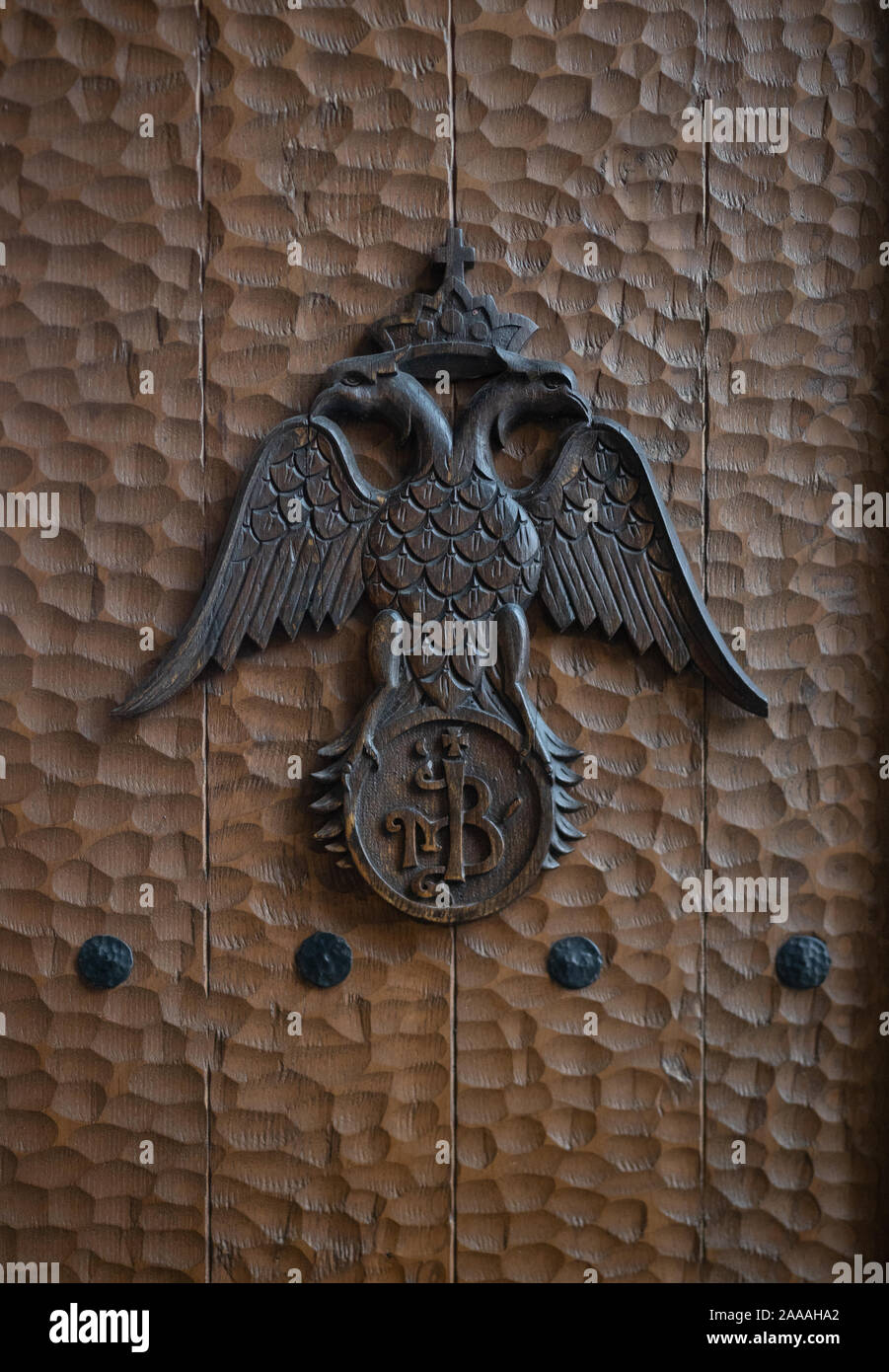 Un aigle aux ailes déployées portant une couronne d'une croix sur une porte en bois martelé. Banque D'Images
