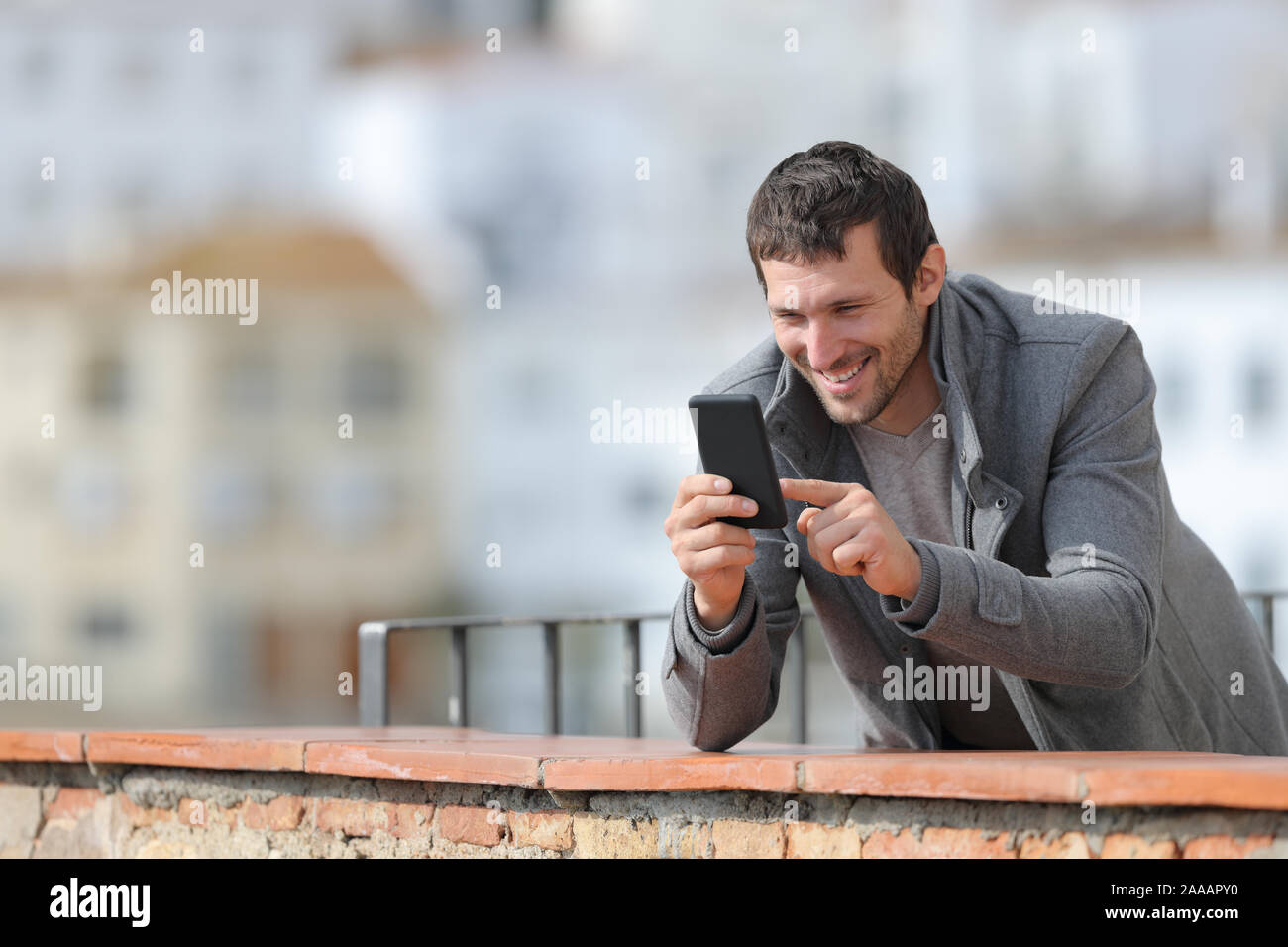 Heureux homme adulte en hiver à l'aide de mobile phone debout dans un balcon en plein air dans une ville rurale Banque D'Images