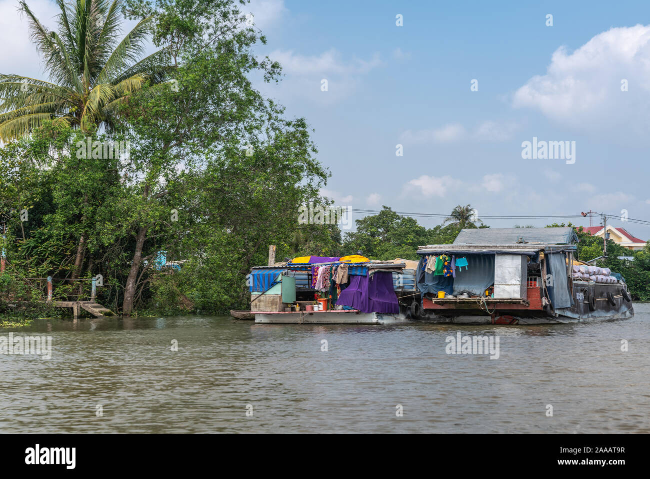 À Cai Be, Delta du Mekong, Vietnam - Mars 13, 2019 : le long du canal 28 Kinh. 2 chalands chargés jusqu'à l'ancre sous le feuillage vert cloudscape bleu. Retour de voile Banque D'Images