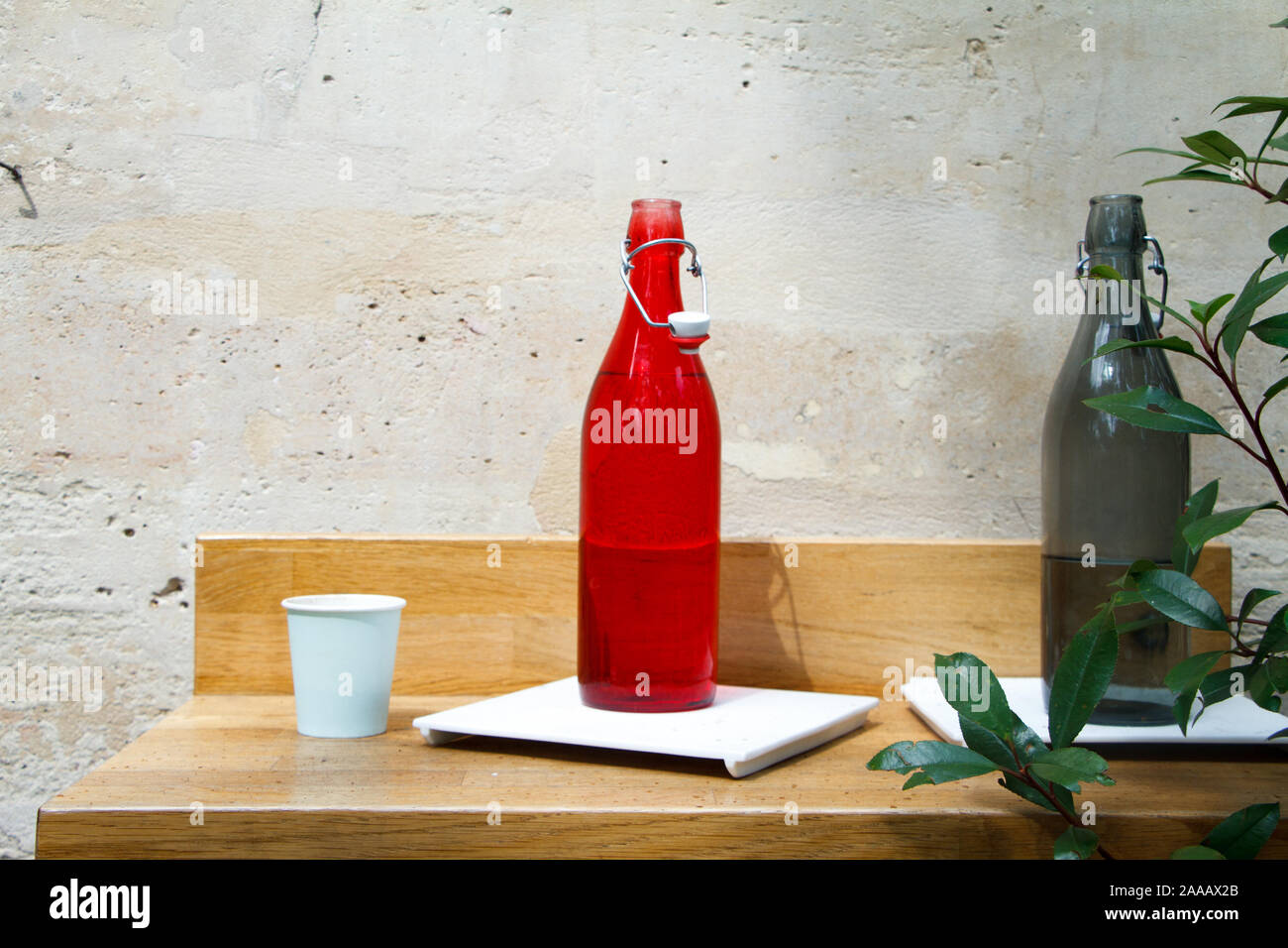 Close-up d'une bouteille d'eau rouge et gris et de verre sur une table de restaurant contre un mur de pierre de lumière Banque D'Images