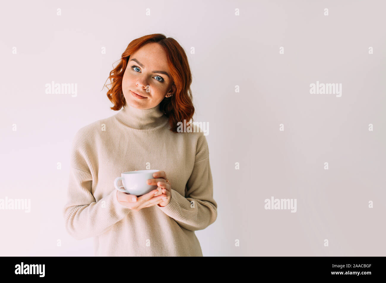 Portrait de vie de femme séduisante aux cheveux rouges de boire du café d'une tasse blanche, le port d'un chandail confortable ton pastel. Banque D'Images