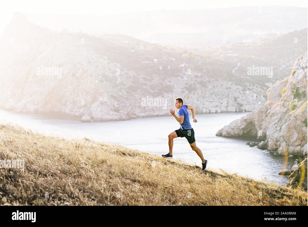 Athlète homme running uphill sur fond de coucher de soleil dans la baie de la mer Banque D'Images