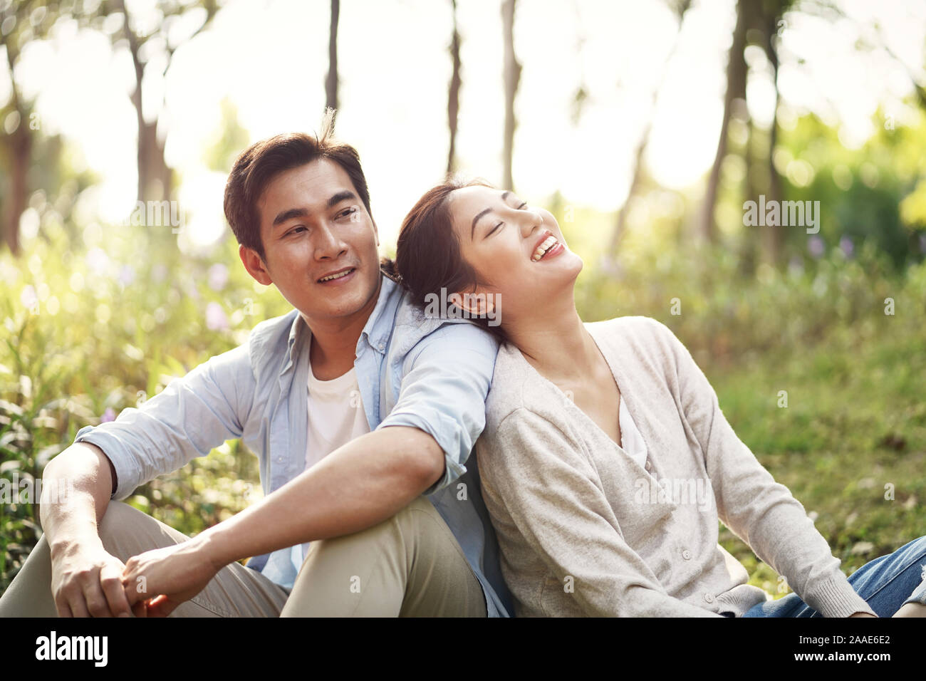 Beautiful happy young asian woman sitting on grass talking chatting relaxing in park Banque D'Images