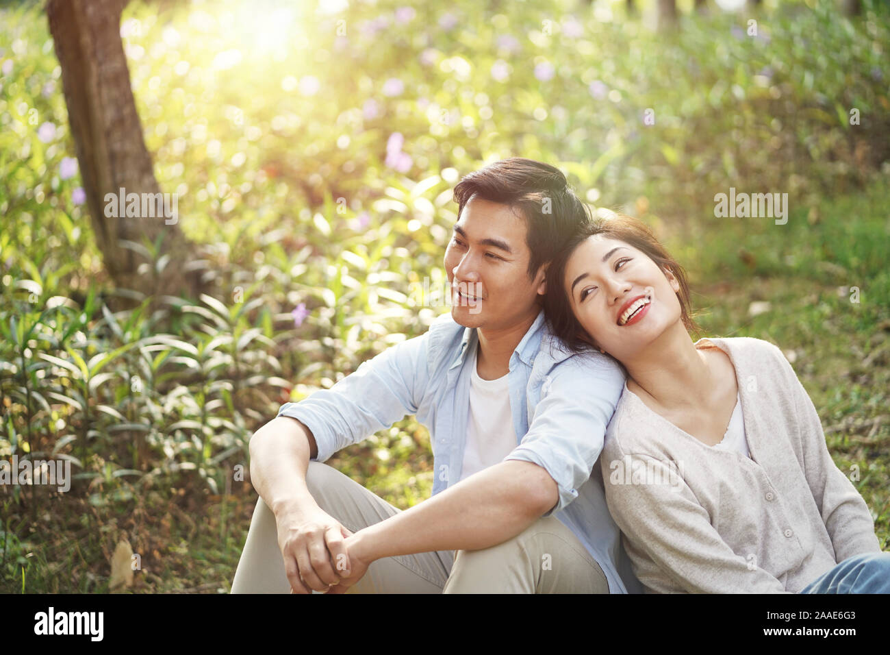 Beautiful happy young asian woman sitting on grass talking chatting relaxing in park, high angle view Banque D'Images