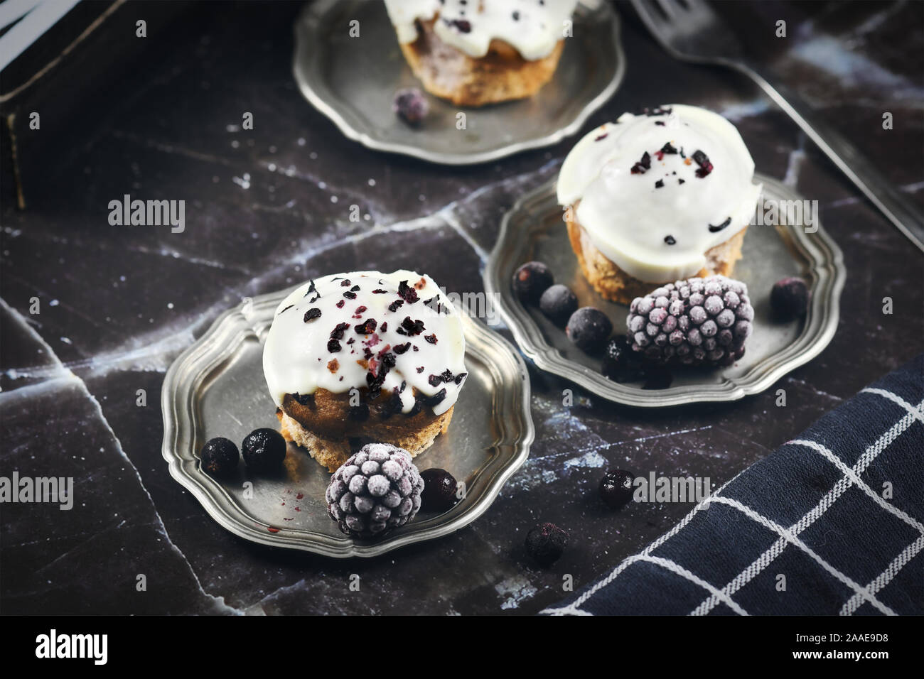 De délicieux muffins aux bleuets avec glaçage au chocolat blanc décorée sur les plateaux en étain avec des baies sur backgrund de marbre noir Banque D'Images