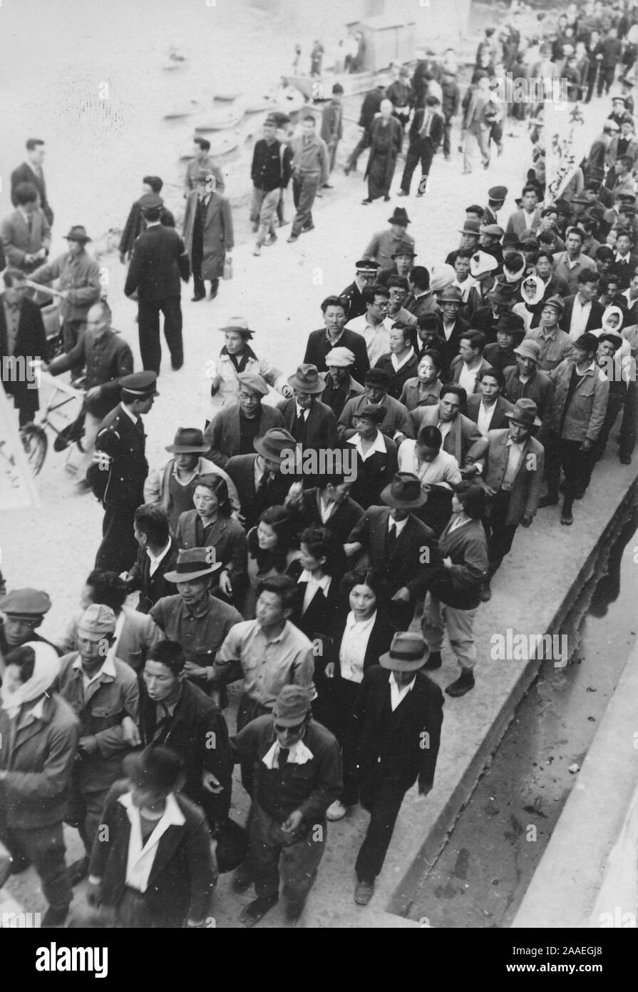 Bird's-eye shot des passants et des policiers de regarder une longue colonne de manifestants, beaucoup d'armes, liés à marcher sur un pont ou un quai pendant le travail Union européenne des protestations, la Préfecture de Fukuoka, Japon, 1950. () Banque D'Images