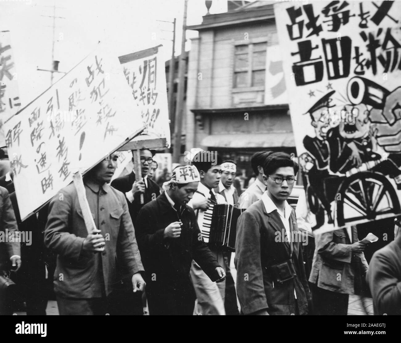 Vue de profil d'une foule de travailleurs, y compris un jeune homme au premier plan à l'égard de l'appareil photo, marchant avec des signes lors d'une manifestation syndicale du travail, la Préfecture de Fukuoka, Japon, 1950. () Banque D'Images