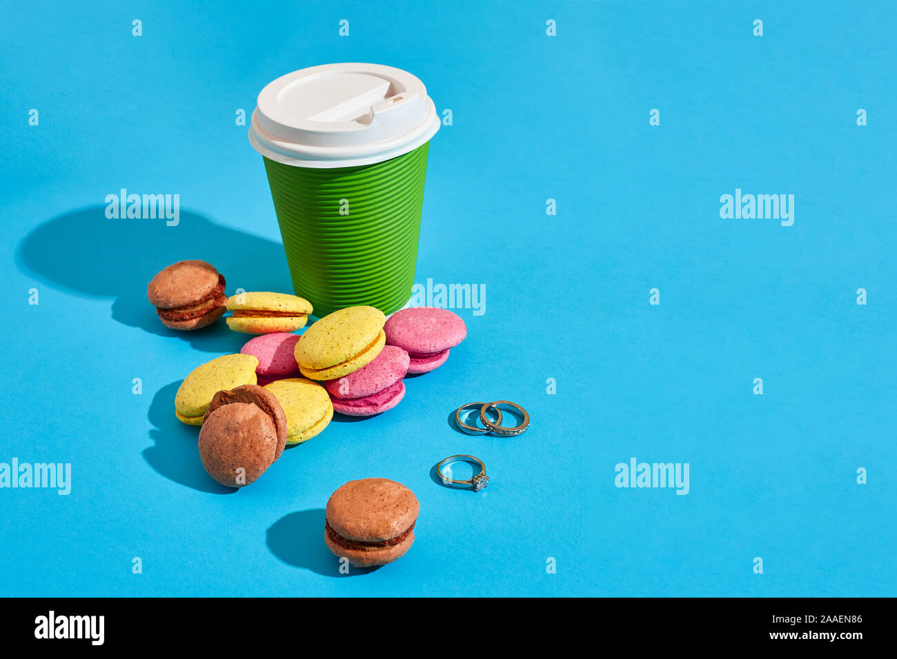 Café chaud dans la tasse de papier vert avec couvercle blanc et macarons sur bl Banque D'Images