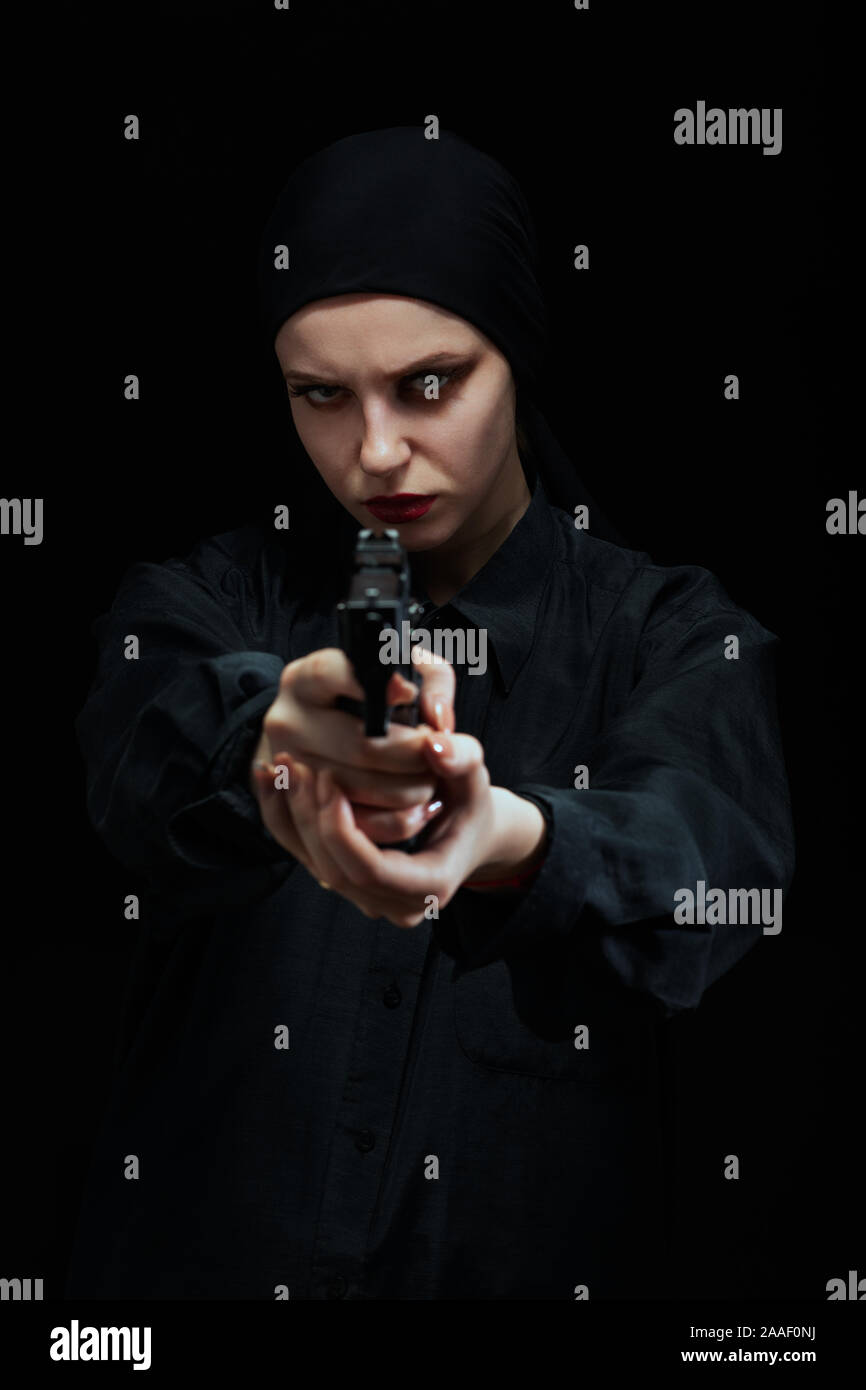 Jeune fille sérieuse avec arme visant à huis clos sur fond noir Banque D'Images