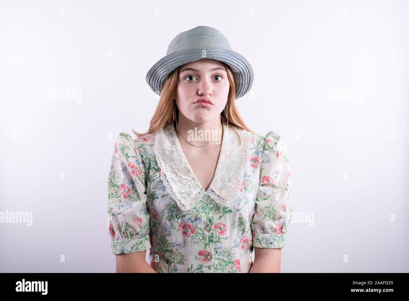 Portrait of teenage girl wearing a vintage robe et chapeau bleu avec ennuie regard sur son visage sur un fond blanc. Banque D'Images