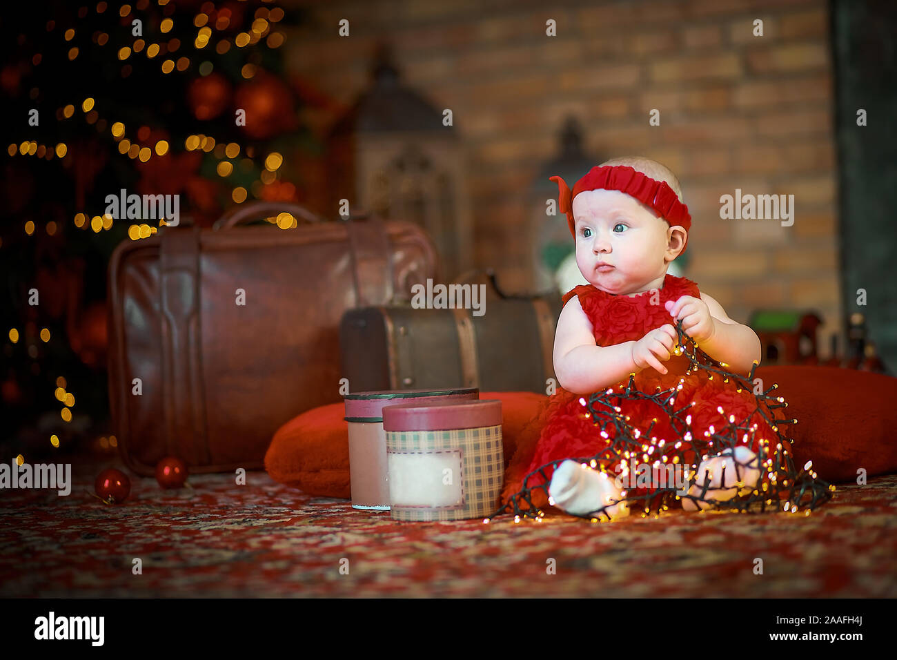 Petite fille en robe rouge à l'arrière-plan de Noël arbre de Noël est titulaire d'garland en mains. bébé 6 mois fête Noël. Jouets dangereux. Banque D'Images