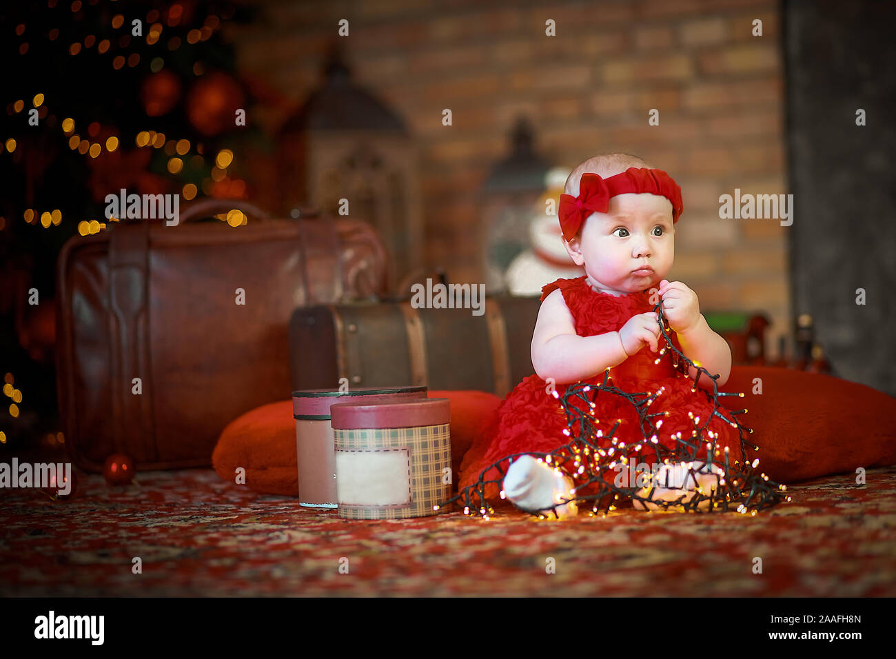 Petite fille en robe rouge à l'arrière-plan de Noël arbre de Noël est  titulaire d'garland en mains. bébé 6 mois fête Noël Photo Stock - Alamy
