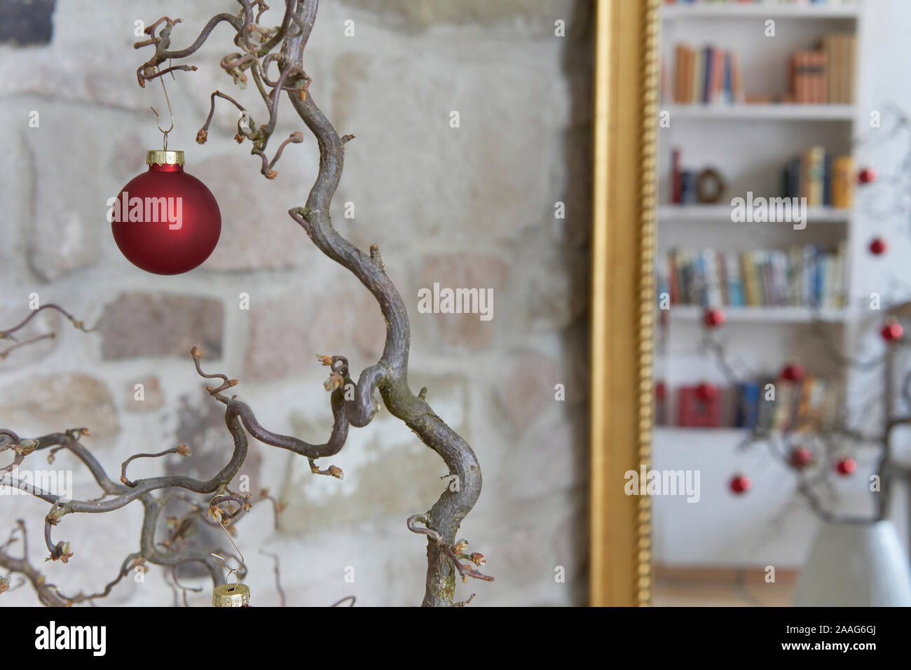 Gros plan d'une boule de noël rouge à une branche en face de mur de pierre en flou un loft et réflexions avec miroir Banque D'Images