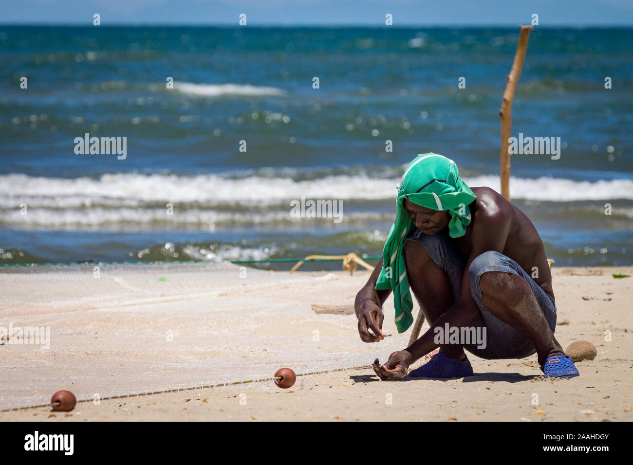 Un homme seul sur la rive du lac Malawi raccommode son filet de pêche Banque D'Images