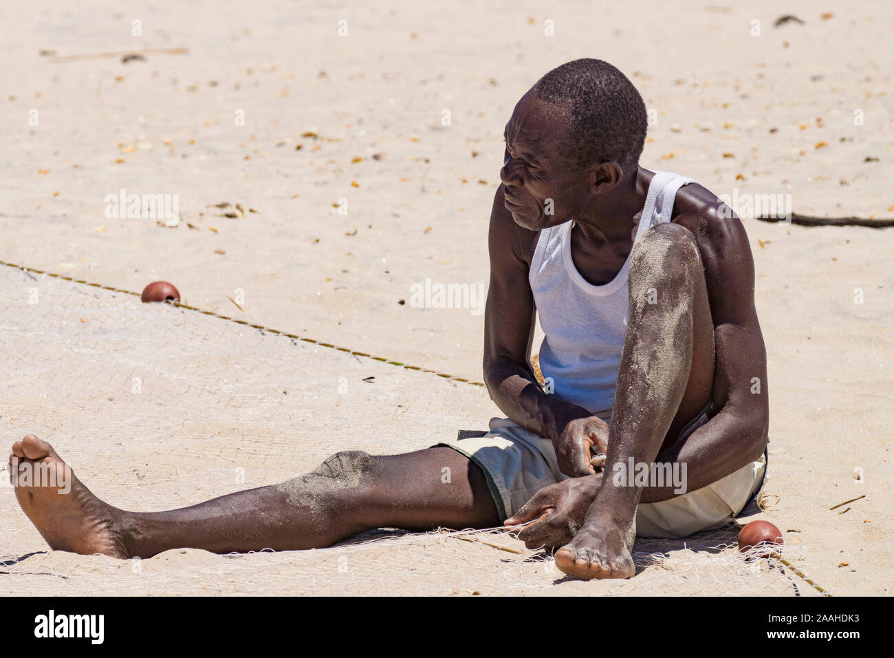 Un homme seul sur la rive du lac Malawi raccommode son filet de pêche Banque D'Images