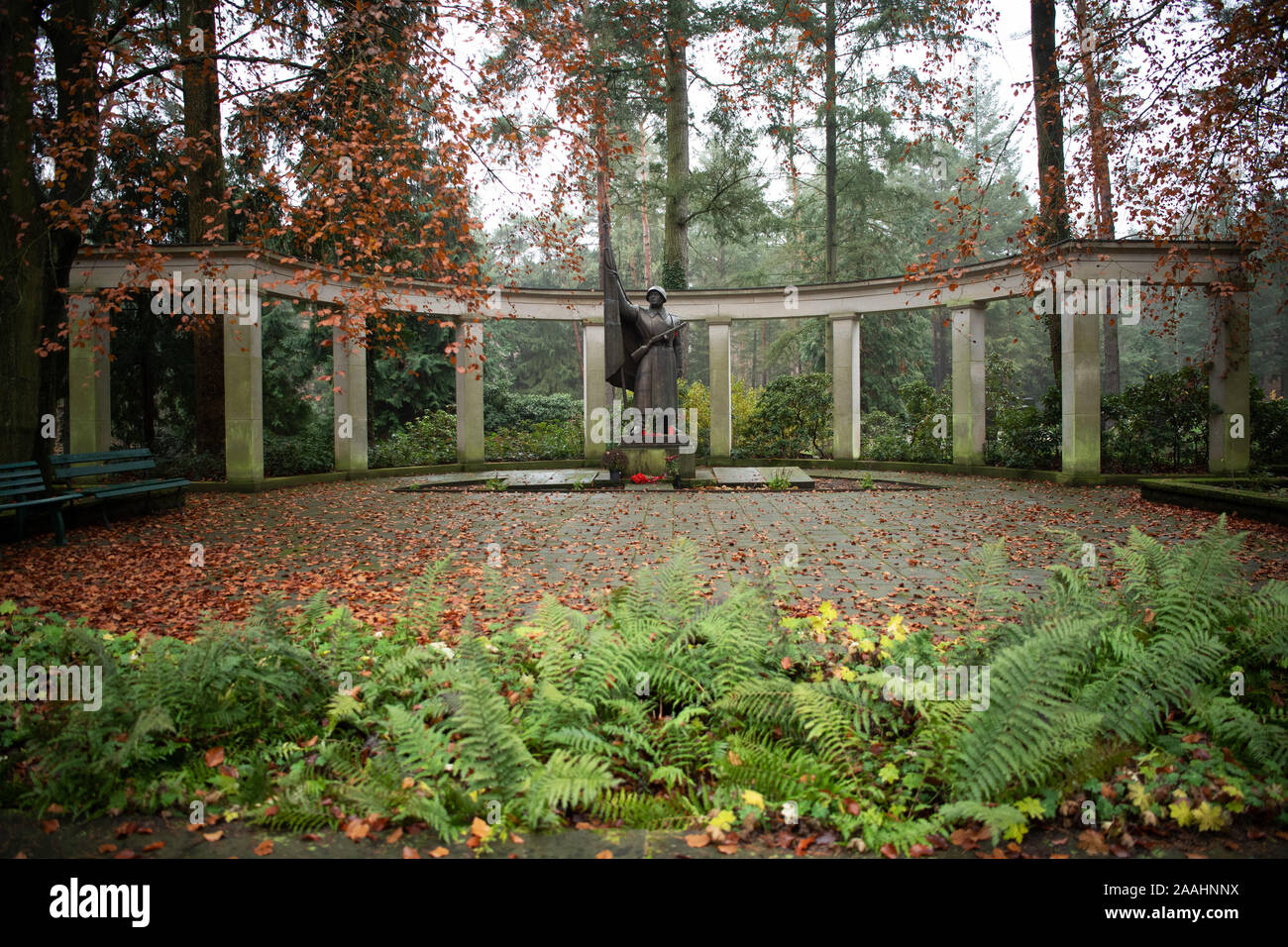 21 novembre 2019, Brandenburg, Potsdam : La sculpture de bronze 1957 'Smit Fahne' (avec le drapeau "soldat"), conçu par le sculpteur Walter Bullert en 1953 à la fonderie, Dresden se trouve en face d'une pergola sur le cimetière soviétique dans une zone boisée sur Bundesstraße 2 entre Potsdam et Michendorf. Sur 39 lieux de sépulture 2399 morts de guerre soviétique de la Seconde Guerre mondiale et 2829 policiers, les militaires, les employés civils et les officiers de la garnison de l'armée soviétique en RDA sont enterrés. Dans certaines tombes il y a des photos de la personne décédée, une tradition qui est commun en Russie. Autre pierre tombale Banque D'Images