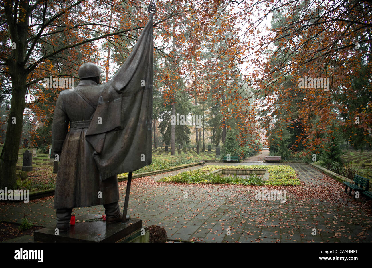 21 novembre 2019, Brandenburg, Potsdam : La sculpture de bronze 1957 'Smit Fahne' (avec le drapeau "soldat"), conçu par le sculpteur Walter Bullert en 1953 à la fonderie, Dresden se trouve en face d'une pergola sur le cimetière soviétique dans une zone boisée sur Bundesstraße 2 entre Potsdam et Michendorf. Sur 39 lieux de sépulture 2399 morts de guerre soviétique de la Seconde Guerre mondiale et 2829 policiers, les militaires, les employés civils et les officiers de la garnison de l'armée soviétique en RDA sont enterrés. Dans certaines tombes il y a des photos de la personne décédée, une tradition qui est commun en Russie. Autre pierre tombale Banque D'Images