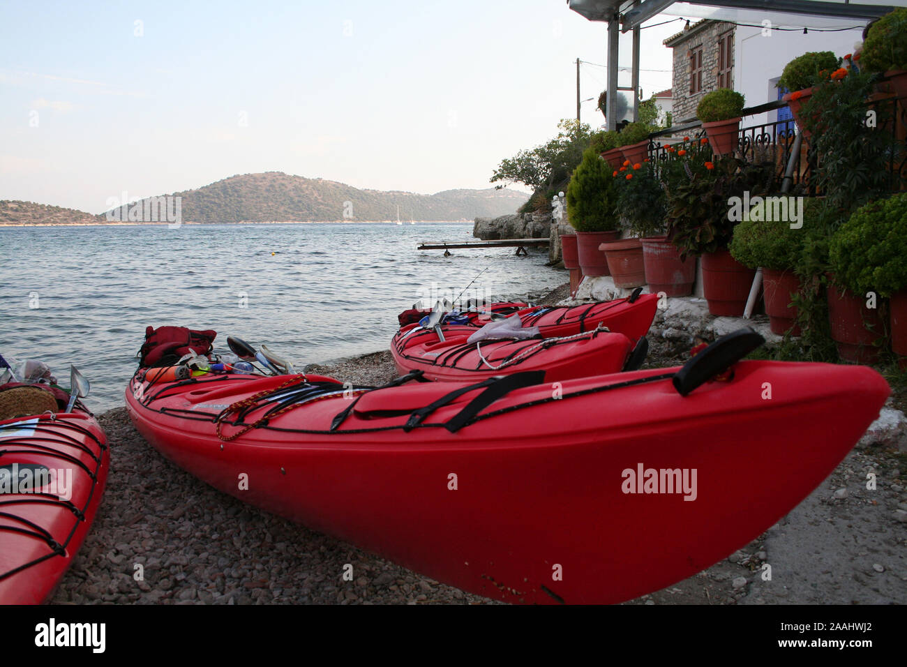Kayaks de mer sur le rivage, fleurs en arrière-plan et taverne, îles lointaines, kayaks rouges sur la plage avec mer et îles à distance Banque D'Images