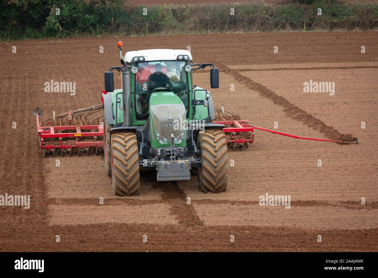 Agriculteur à l'œuvre l'ensemencement de graminées fourragères pour la nouvelle saison, à l'aide d'un semoir semoir ou à Cornwall en Angleterre. Banque D'Images