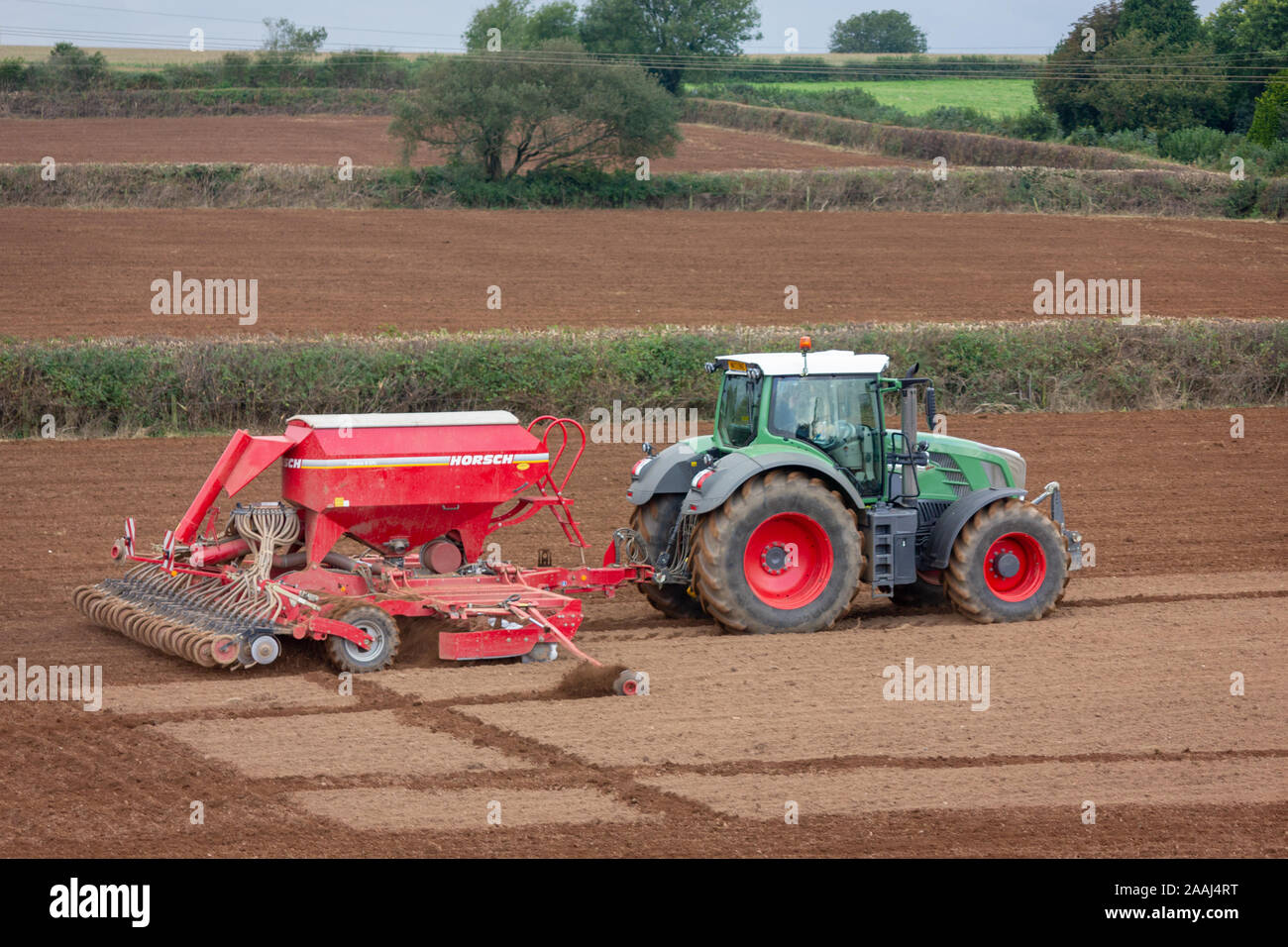 Agriculteur à l'œuvre l'ensemencement de graminées fourragères pour la nouvelle saison, à l'aide d'un semoir semoir ou à Cornwall en Angleterre. Banque D'Images