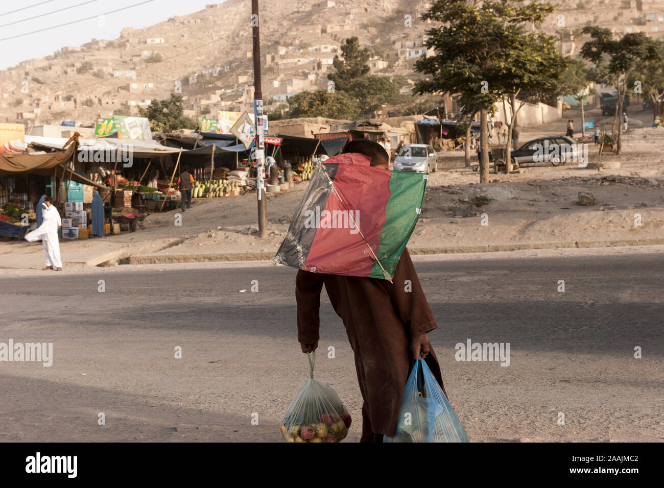 Un jeune garçon avec un cerf-volant sur le dos, traverse la rue des sacs  d'épicerie, à Kaboul, Afghanistan Photo Stock - Alamy