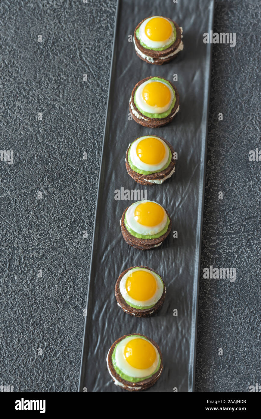 Canape avec fromage à la crème, guacamole et oeufs de caille frit sur la plaque Banque D'Images