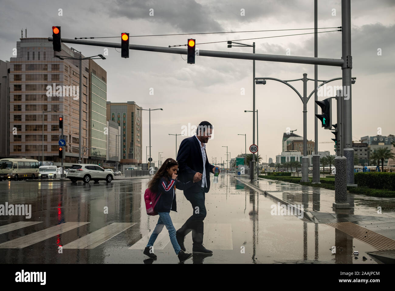 Père et fille traverser la route alors que pleuvoir à Abu Dhabi, Émirats arabes unis Banque D'Images