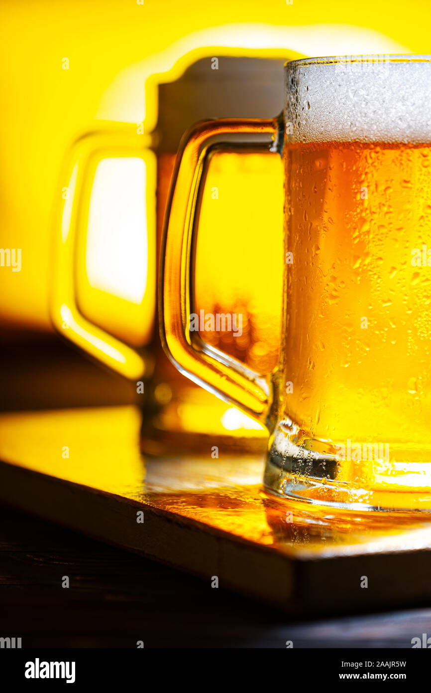 Deux verres avec mousse blanche sur table en bois sombre et fond jaune Banque D'Images