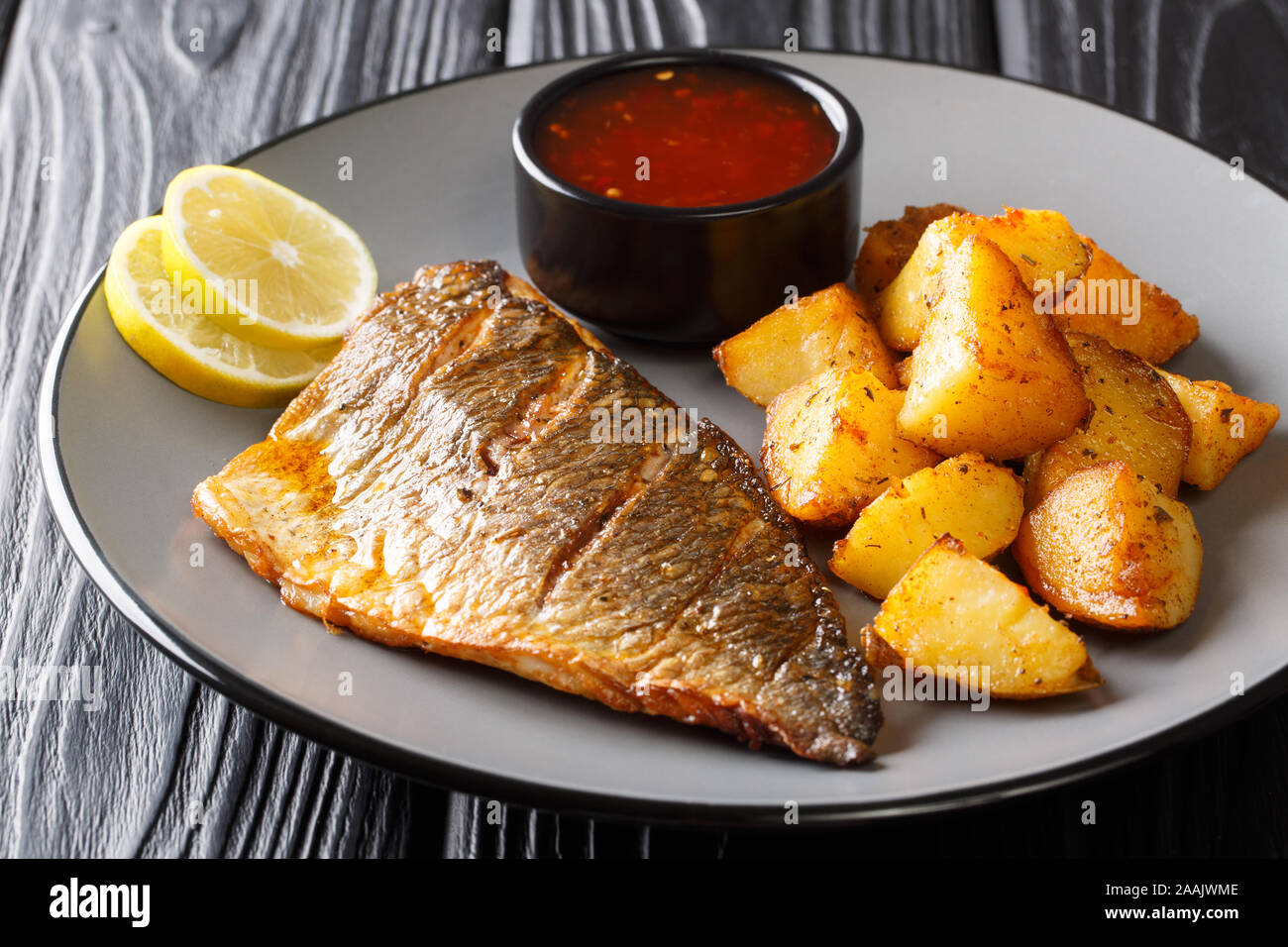 Filet de poisson frit délicieux dorado avec garniture de pommes de terre et sauces close-up sur une plaque sur la table horizontale. Banque D'Images