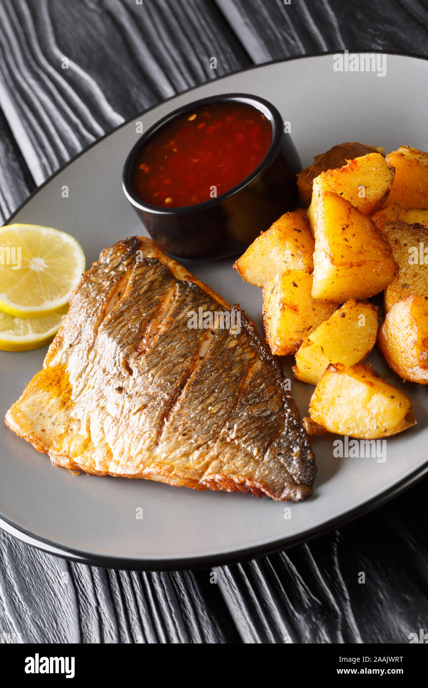 Filet de dorade poêlé avec des pommes de terre et sauces close-up sur une plaque verticale sur la table. Banque D'Images