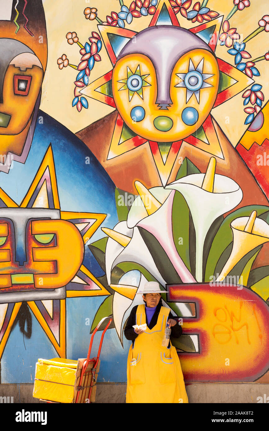 Une femme avec une bouteille d'eau à côté d'un mur recouvert de peintures murales traditionnelles à La Paz, Bolivie. La Paz est désespérément à court d'eau comme les glaciers o Banque D'Images