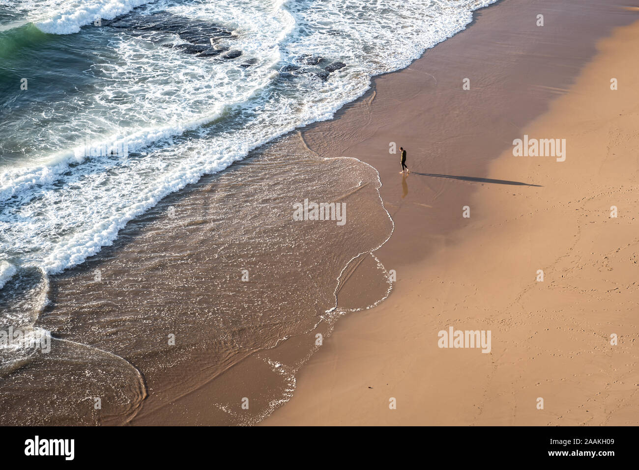Matériel roulant dans les vagues à |côte atlantique avec plage vide avec un casting long shadow walker pieds nus sur le sable en Praia das Maçãs au Portugal Banque D'Images