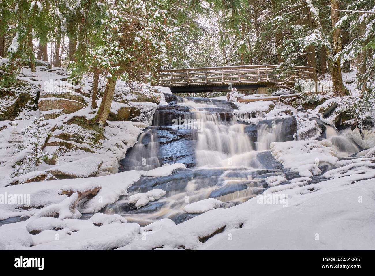 Après la première chute de neige de la saison, l'eau passe sous une passerelle et tombe sur les roches du Bouclier canadien de Potts Falls à Muskoka. Banque D'Images