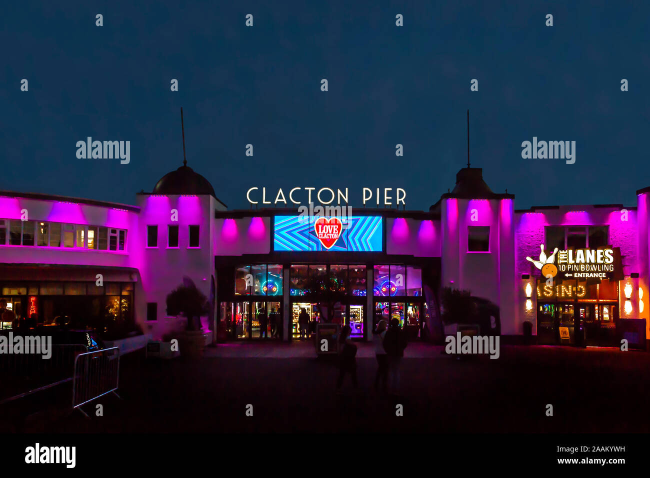 Les gens qui se profile devant l'entrée de la jetée de Clacton dans la nuit. La façade est éclairée par des lumières vives. Banque D'Images