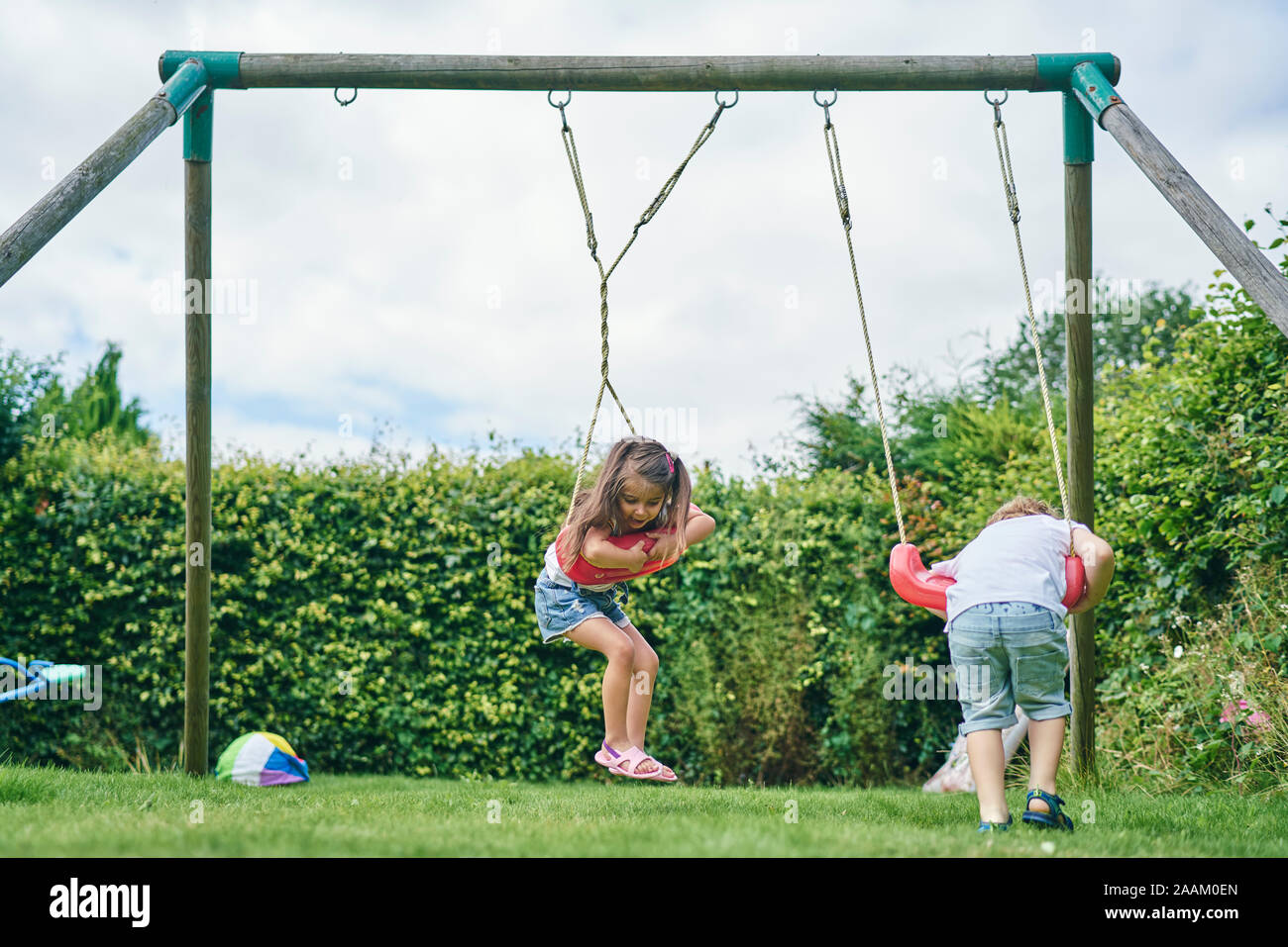 Fille et garçon se tordant autour sur des balançoires dans le jardin Banque D'Images