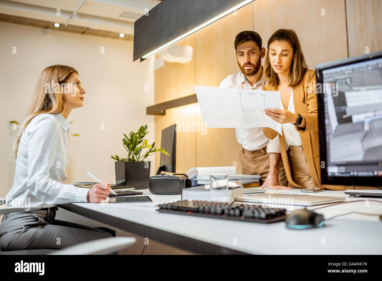 Les jeunes employés habillés à la légère de faire certains travaux de création à la grande table avec les ordinateurs dans le bureau. Concept d'une entreprise d'architecture et de création Banque D'Images