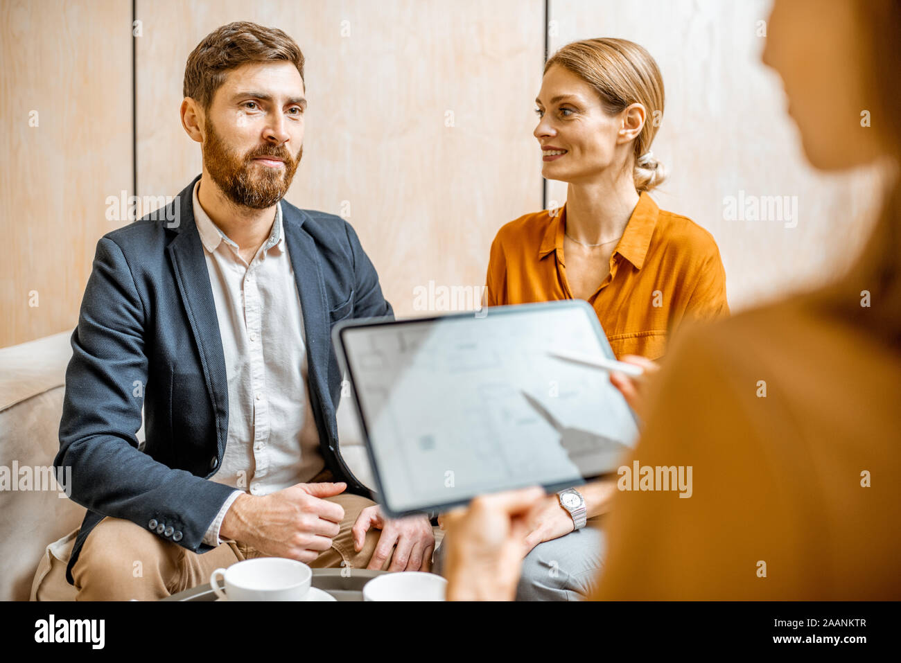Jeune couple de parler avec un directeur des ventes ou agent immobilier, offrant des produits avec une tablette numérique dans l'office Banque D'Images